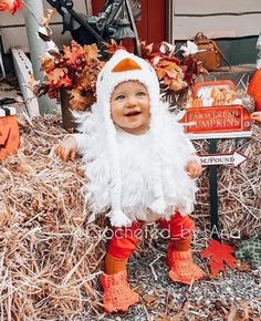 a baby dressed up as a chicken sitting in hay next to a sign and pumpkins