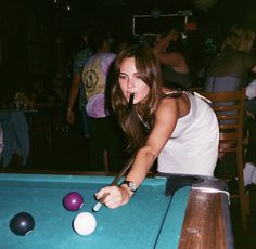 a woman leaning over a pool table to hit a ball with a cue in her hand