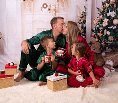 a man and woman kiss their children as they sit on the floor with presents in front of them