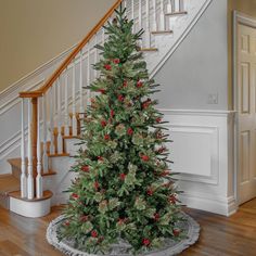 a decorated christmas tree sitting in the middle of a living room next to a stair case