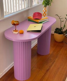 a purple table with books and an orange on it next to a potted plant