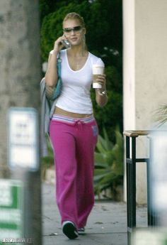 a woman is walking down the sidewalk talking on her cell phone and holding a cup of coffee