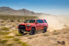 a red toyota 4runner driving down a dirt road