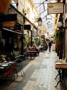 an alley way with tables and chairs on both sides, people walking down the street