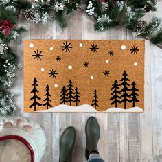 a person standing in front of a door mat with snowflakes and trees on it