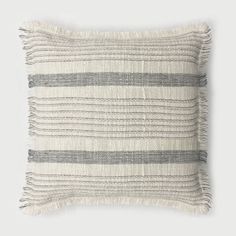 a gray and white striped pillow with fringes on the front, sitting on a grey background