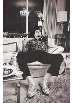 a man sitting on top of a couch holding up a bottle in his right hand