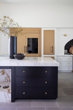 a large kitchen with marble counter tops and black cabinetry, along with a vase on the island