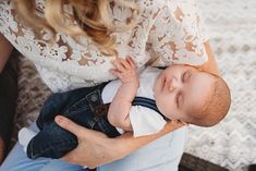 a woman holding a baby in her lap while he is wearing a white shirt and blue jeans