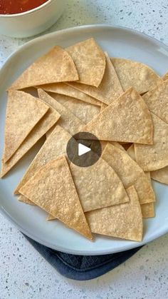 tortilla chips on a white plate with dipping sauce in the bowl behind them