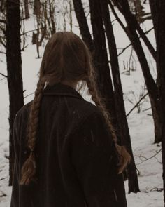 a girl with braids standing in the snow near some trees and looking at something