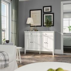 a white dresser sitting in a living room next to a lamp and pictures on the wall