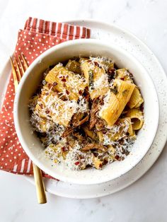 a white bowl filled with pasta and cheese on top of a red napkin next to a fork