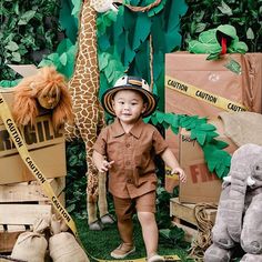 a little boy standing in front of stuffed giraffes and other toys at a jungle themed birthday party