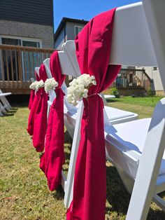 white chairs with red sashes and flowers tied to them are lined up on the grass