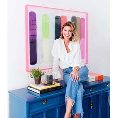 a woman sitting on top of a blue cabinet in front of a colorful wall hanging