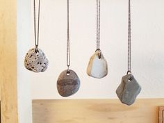 four stone pendants hanging from chains on a wooden shelf in front of a white wall