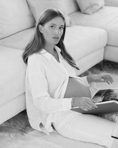 a woman is sitting on the floor reading a book and looking at the camera, black and white photo