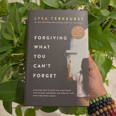 a person holding up a book in front of a plant with green leaves on it