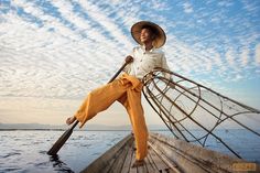 a woman in a straw hat is sitting on a boat and holding a long oar