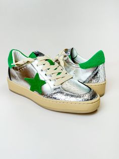 a pair of silver and green sneakers with stars on them, sitting on a white surface