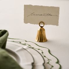 a place card holder with a gold bell on it and a green napkin next to it