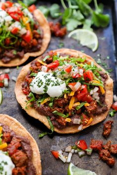 three tacos on a baking sheet with limes, cilantro and sour cream