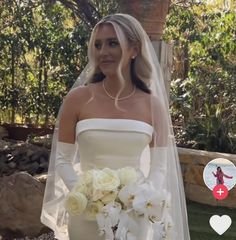 a woman in a white wedding dress holding a bouquet of flowers and wearing an arm length veil