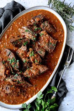 beef stew in a white bowl with garnishes and herbs on the side