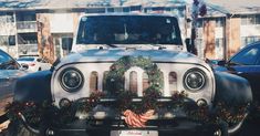 an old jeep decorated for christmas with wreaths on the grill and front bumper wheel