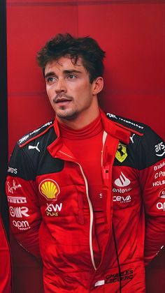 a man in a red racing suit standing next to a red wall with his hands on his hips