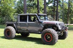 a gray jeep with red wheels parked in the grass next to some trees and bushes