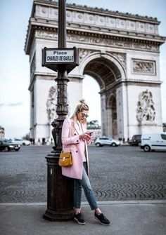 a woman leaning against a lamp post in front of the arc de trioe