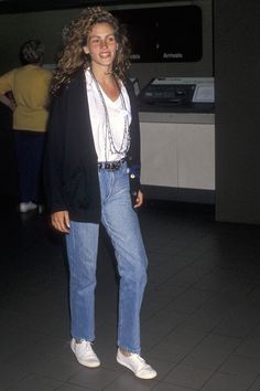 a woman standing in an airport wearing jeans and a blazer