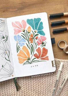 an open notebook with watercolor flowers on it next to markers and crayons