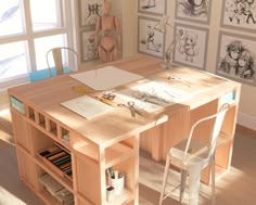 a wooden desk topped with lots of books and art supplies next to a window filled with drawings