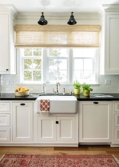 a kitchen with white cabinets and black counter tops, an area rug and two lights above the sink