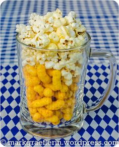 a glass mug filled with popcorn on top of a checkered table cloth