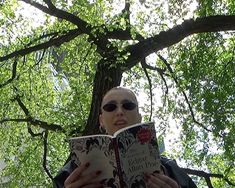 a woman reading a book under a tree in the sun with shades on her face