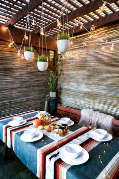 a table with plates and bowls on it in front of a bamboo wall covered by lights