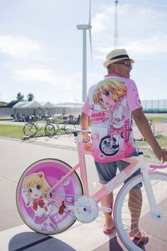 a man standing next to a pink bike on the side of a road with anime characters painted on it