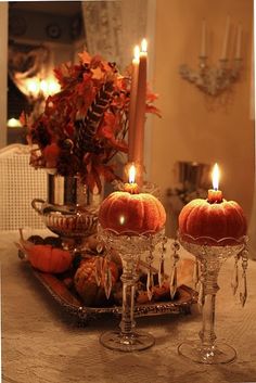 two pumpkins are sitting in wine glasses on a table with candles and other decorations