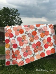 an orange and gray quilt hanging on a wooden fence in the middle of a field