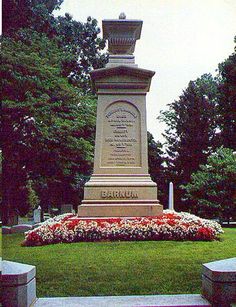 a monument in the middle of a park with flowers around it and trees behind it