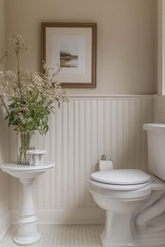 a white toilet sitting next to a sink in a bathroom under a framed picture on the wall