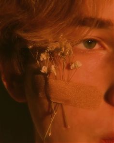 a young man with tape on his nose and flowers in front of his face, looking at the camera