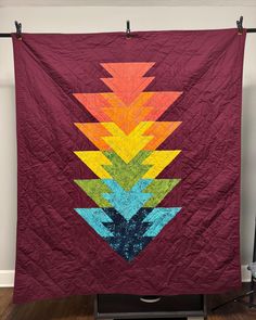 a quilted wall hanging on the side of a wooden floor in front of a white wall