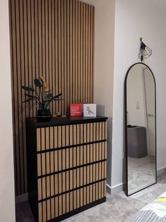 a room with a dresser, mirror and plant on it's side table in front of the wall