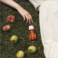 a woman laying in the grass next to some apples and an orange bottle with vitamins on it