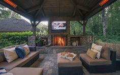 an outdoor living area with couches and a television on the wall, fireplace in the background